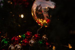 Close-up of a wine glass reflecting holiday ornaments and lights with red and green decorations in the background.