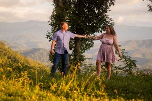 A couple dances together on a mountaintop meadow filled with yellow wildflowers at sunset with mountain views beyond.
