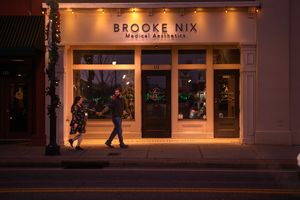 An illuminated storefront exterior with holiday decorations and window displays at night.