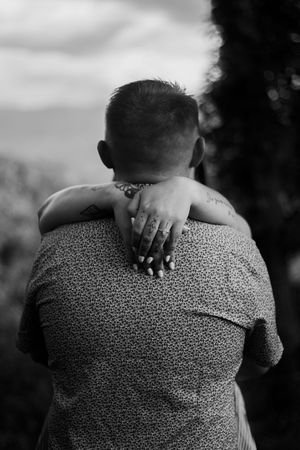 A close-up black and white photo showing hands embracing around shoulders in an intimate moment.