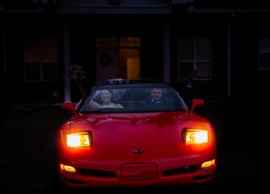 A red Chevrolet Corvette with glowing headlights photographed in low light conditions.