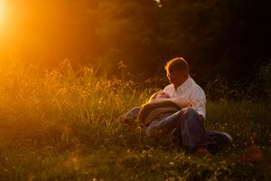 A silhouetted figure stands in a golden meadow at sunset with tall grass and glowing sunlight in the background.