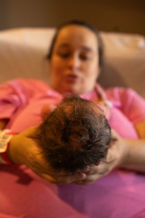 Baby resting on pink bedding with dark curly hair visible.