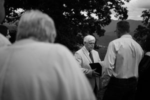 Black and white photo of an outdoor ceremony with people gathered as someone reads from a book.