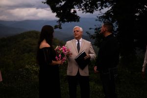 Outdoor wedding ceremony takes place at sunset against a backdrop of mountain scenery and trees.