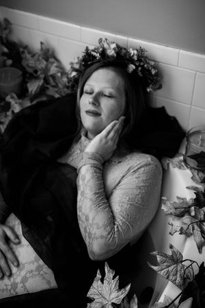 A moody black and white portrait featuring autumn leaves and soft lighting against a white wall.