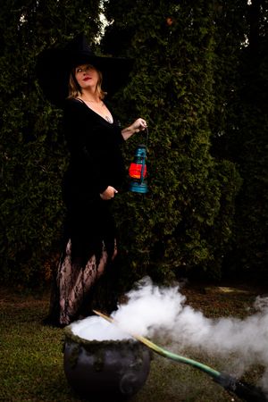 A person in a black dress and red hat releases smoke from a bottle in a dramatic outdoor photo sequence.