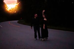 Silhouettes of people walking on a winding mountain road at sunset with dramatic orange sky.
