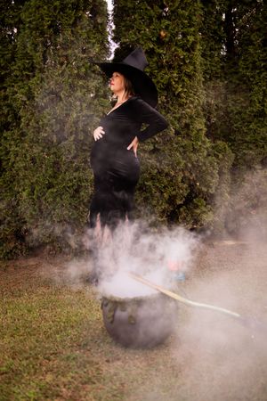 A figure in dark clothing creates mystical smoke effects outdoors against a backdrop of trees and foliage.