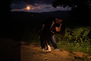 People walking along a curved path at dusk with mountains and moonlit sky in the background.