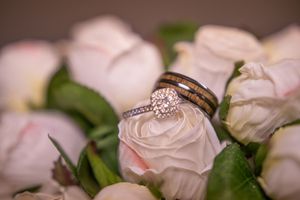 Wedding rings nestled on delicate pink roses with green leaves in a romantic bridal arrangement.