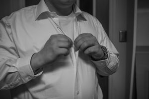 Men in white dress shirts adjusting their ties and cufflinks in a black and white photo.