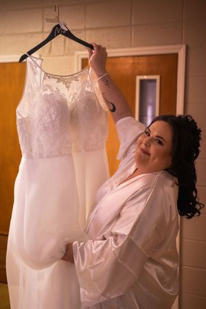 Wedding dress hanging in a warmly lit room while being prepared for the special day.