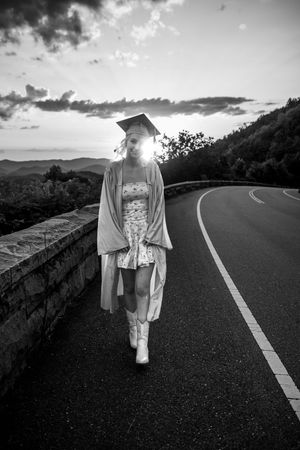 A black and white photo series shows a figure in light clothing walking along a winding mountain road at sunset.