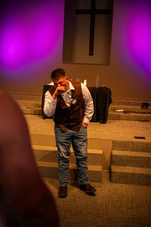 Person kneeling in formal attire against purple-lit backdrop during emotional moment at event.
