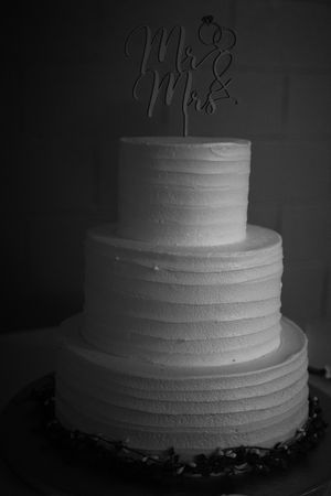 A series of black and white photos showing a tiered white wedding cake with simple textured frosting decoration.