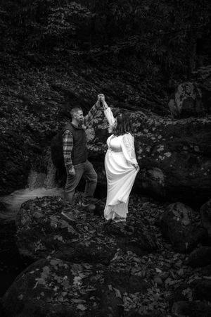 A couple dances together on dark rocky terrain in black and white photography.