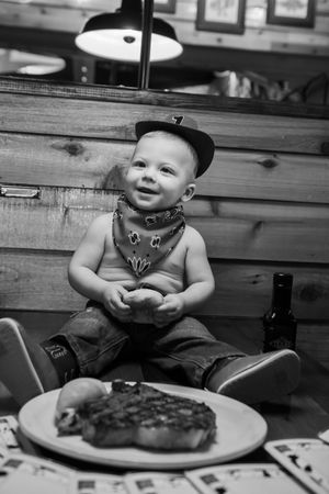 Black and white photo series showing a young child in overalls sitting at a table with food in a rustic setting.