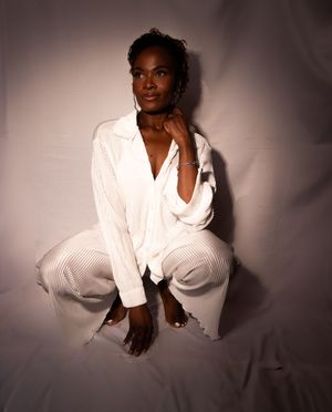 A dramatic studio photoshoot featuring a model in a white shirt against a dark background with artistic lighting.