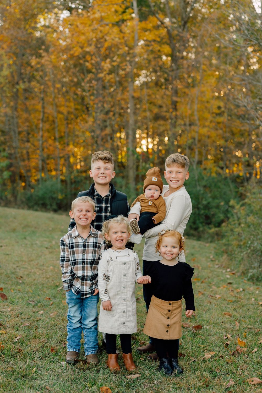 Group of children standing together against autumn foliage backdrop.