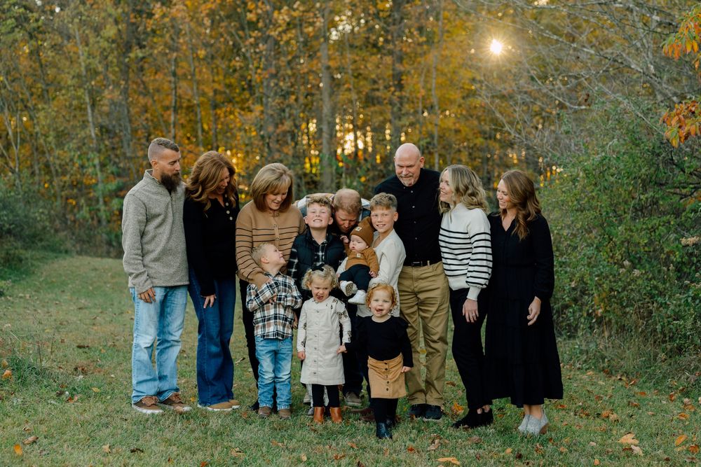 Extended family gathering for portrait in front of autumn trees at sunset.