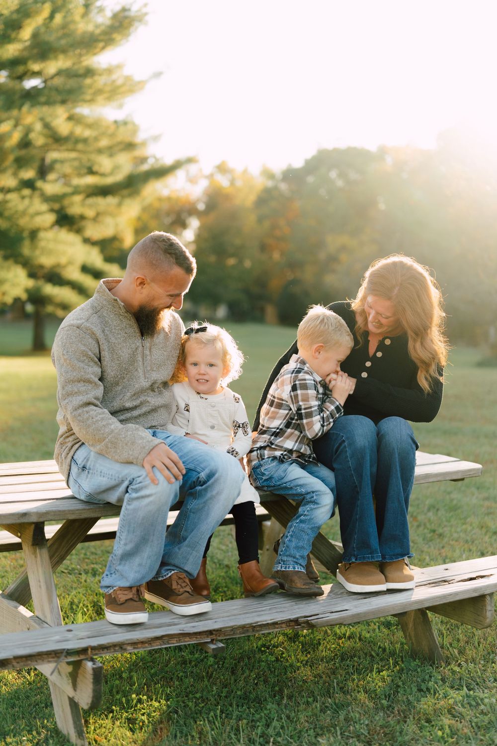 Family sharing tender moments while sitting on wooden picnic bench at sunset.