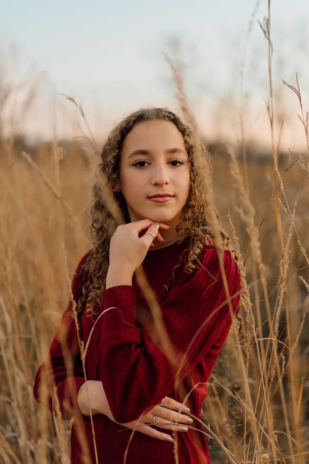 Person in a burgundy sweater poses thoughtfully in a field of tall grass at golden hour in columbus ohio
