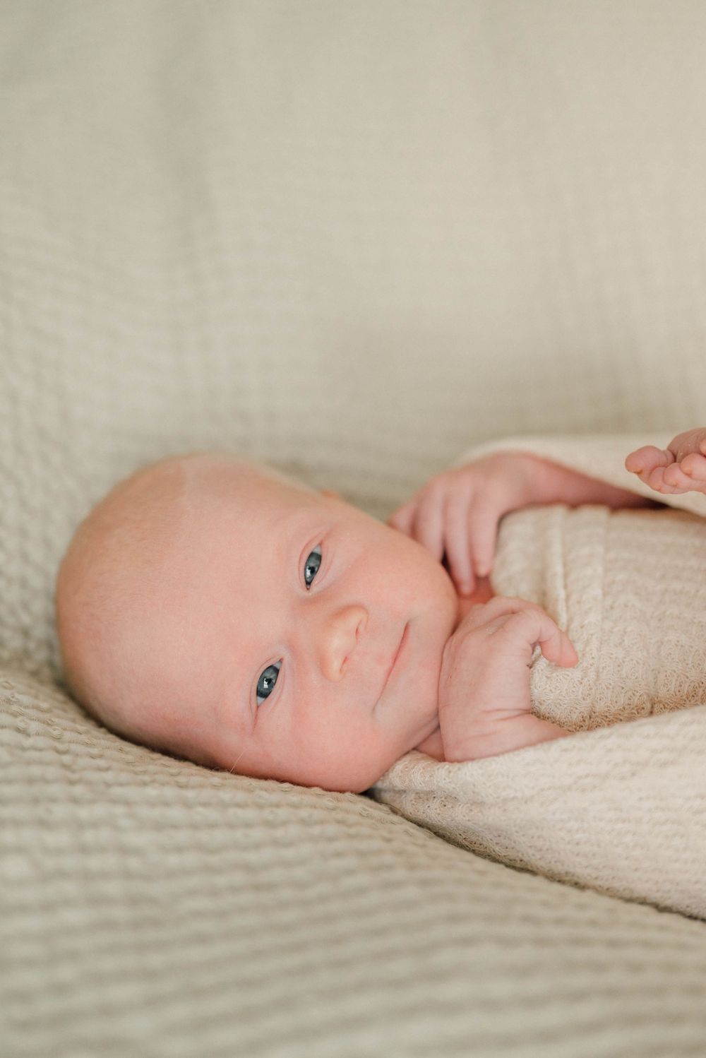 Gentle portrait series of a baby lying on cream textured fabric.