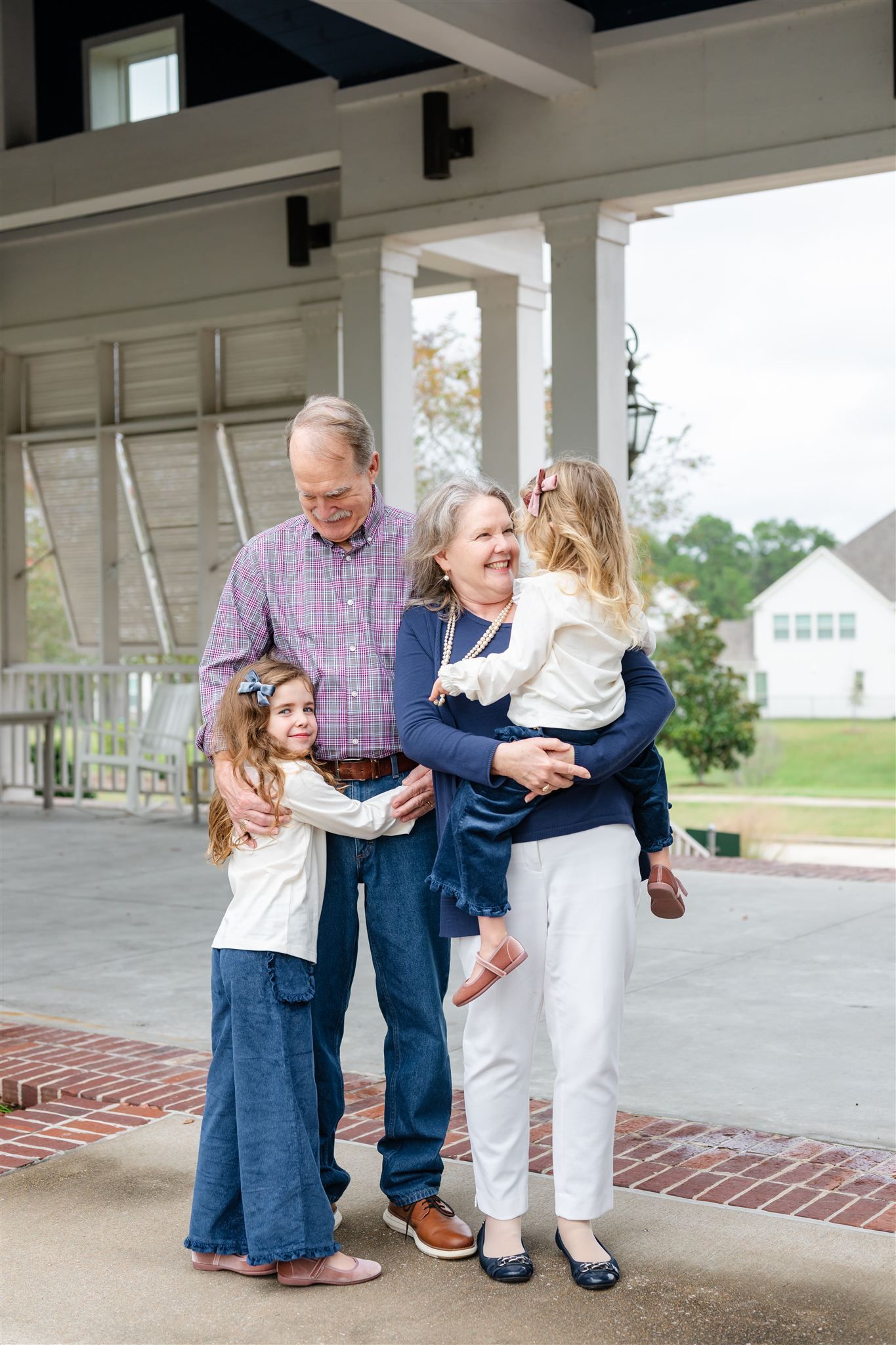 Grandparents and grandchildren embracing and laughing together on a covered porch in Conroe, Tx.