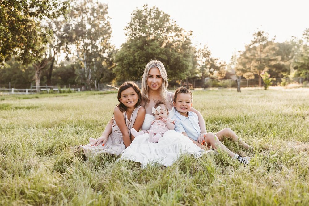 Family lying together in a sunlit grassy field during golden hour photo session.