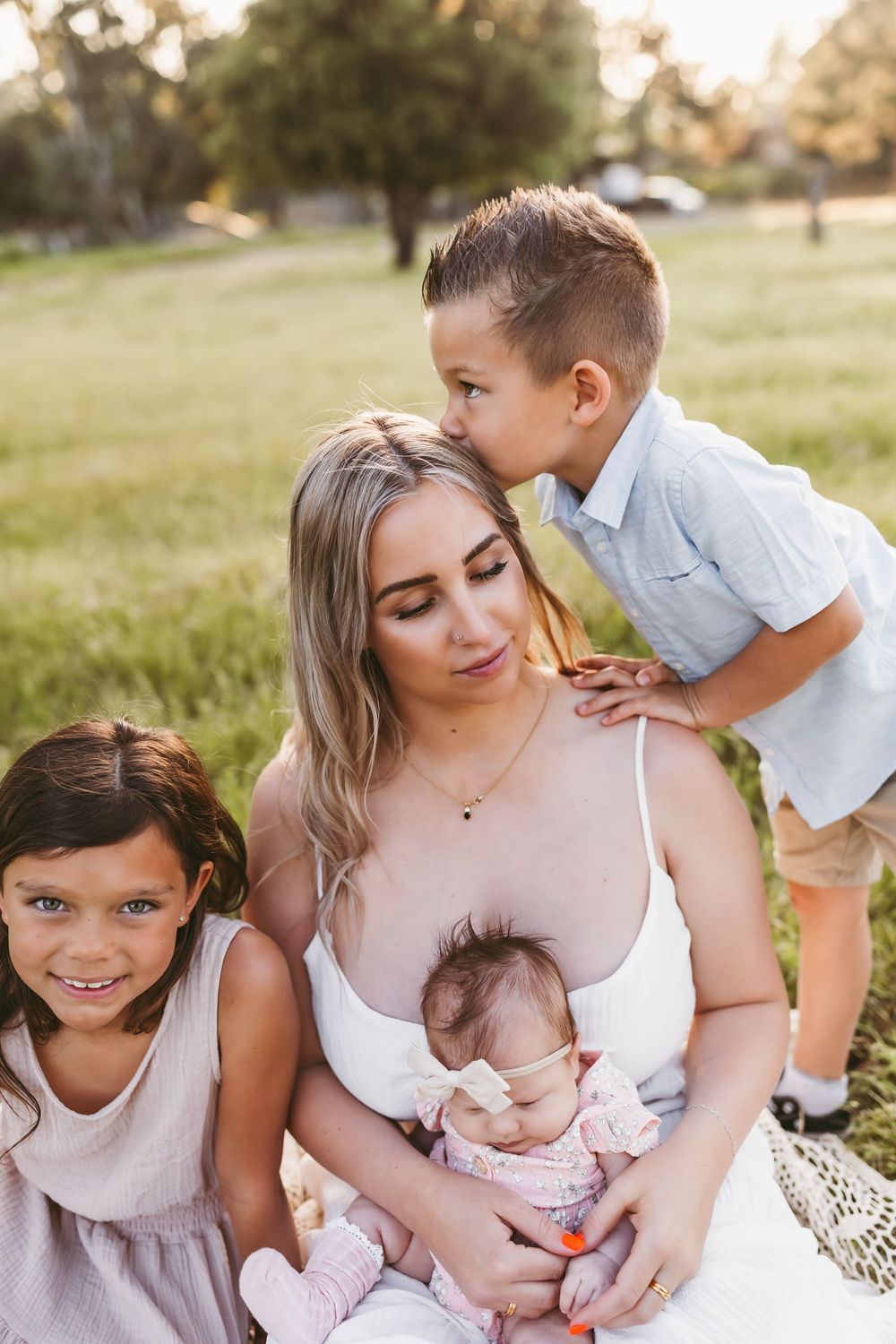 Family in white outfits sharing tender moments together during golden hour outdoor photoshoot.