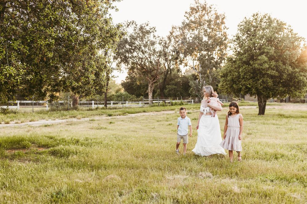 A family walks together through a sunlit grassy field during golden hour.