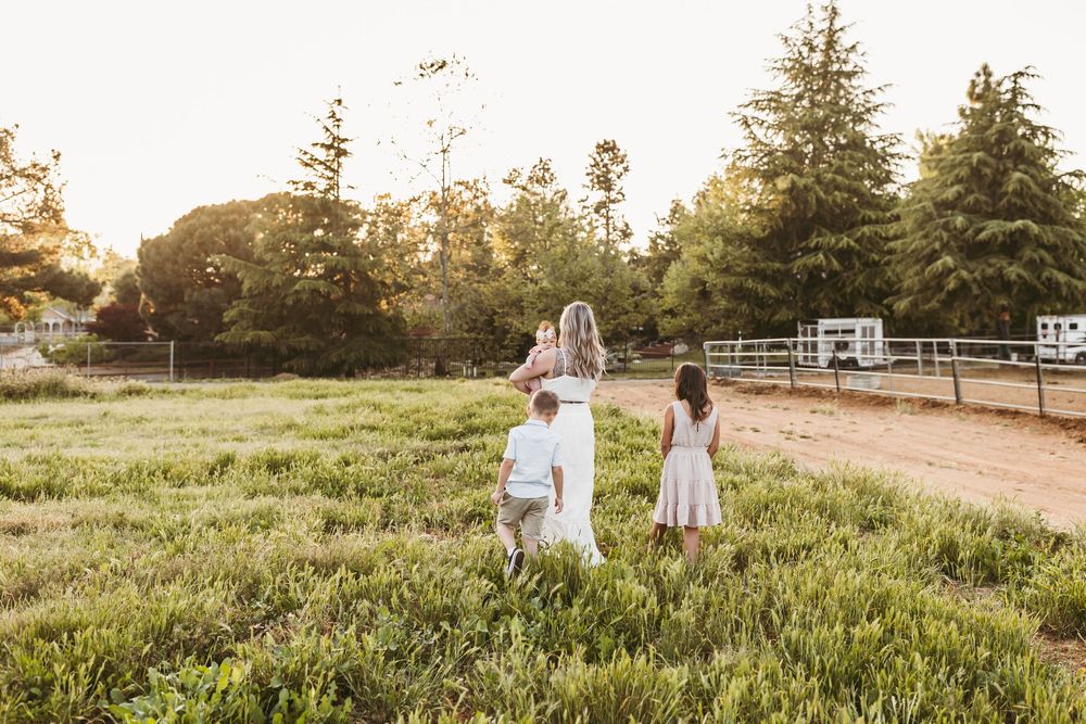 Family members walk along a scenic path with evergreen trees in the background at sunset.