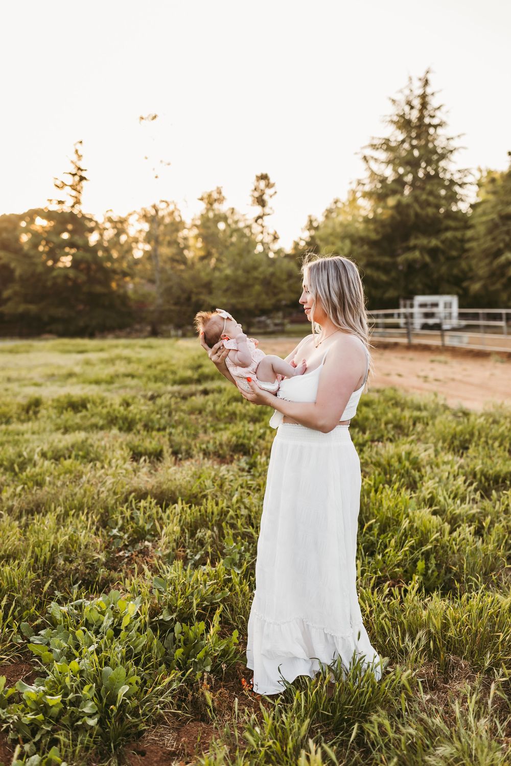 Woman in white dress walking through a sunlit field during a summer evening photoshoot.