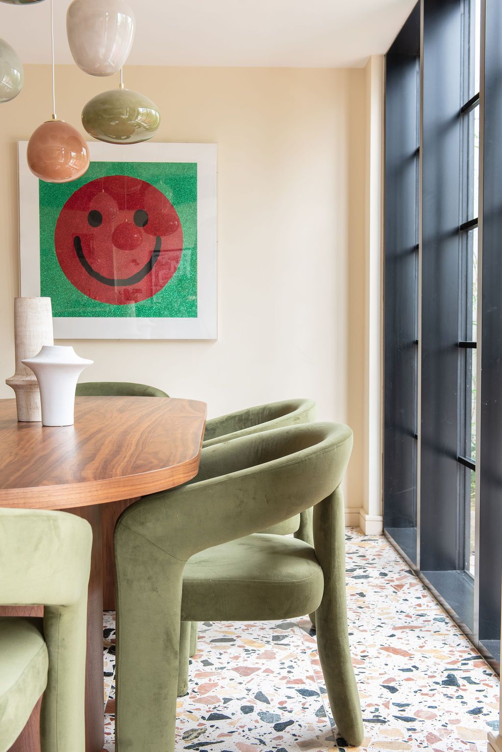 Contemporary dining space with terrazzo floor, olive green barrel chairs, walnut table, and decorative smiley artwork from Saatchi gallery