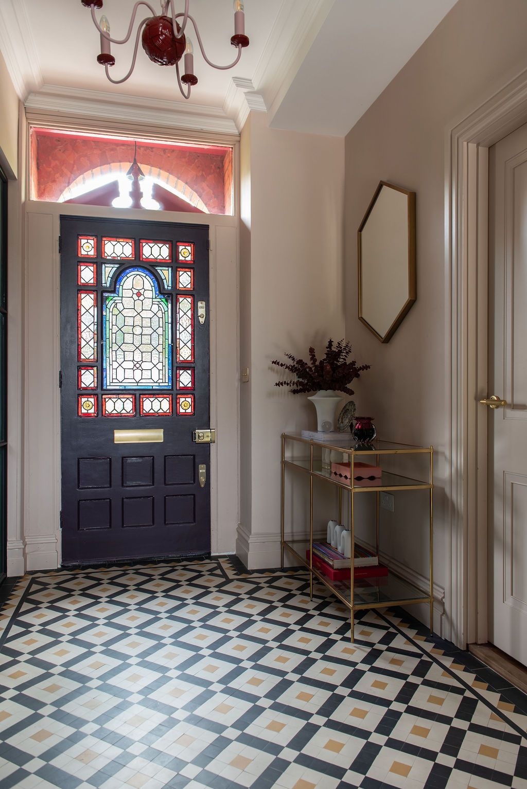 Edwardian elegant entryway with stained glass front door, geometric tile floor, and brass console table against beige walls. Original floor