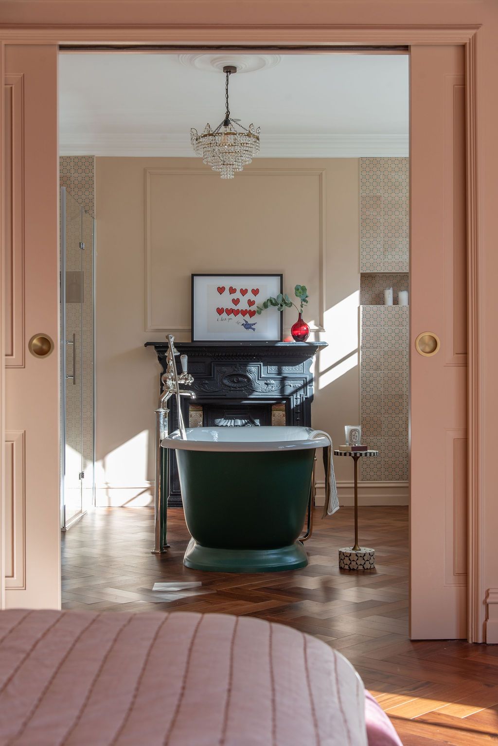 A dark green hot tub sits in an elegant room with hardwood floors and pink walls under natural lighting.
