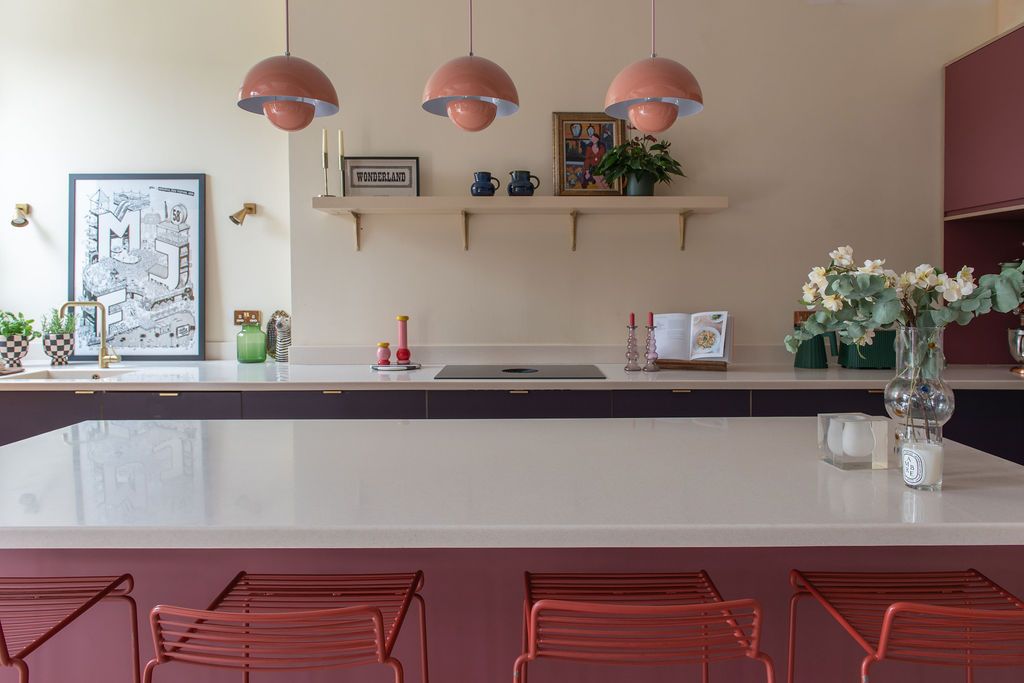 A modern kitchen with red pendant lamps hanging above a long bar counter. Plykea Kitchen