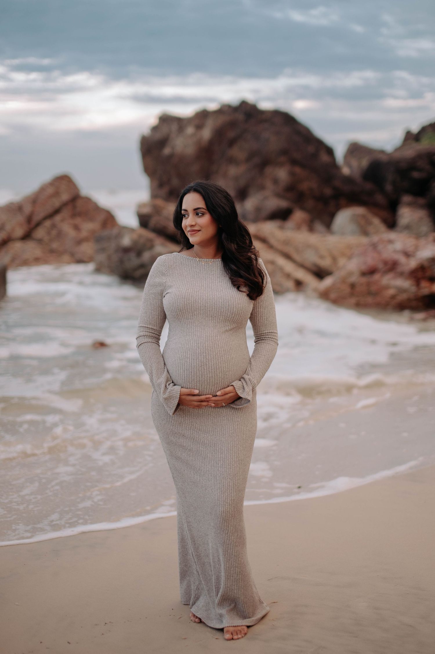 A person in white clothing poses gracefully against dramatic coastal rock formations at sunset.