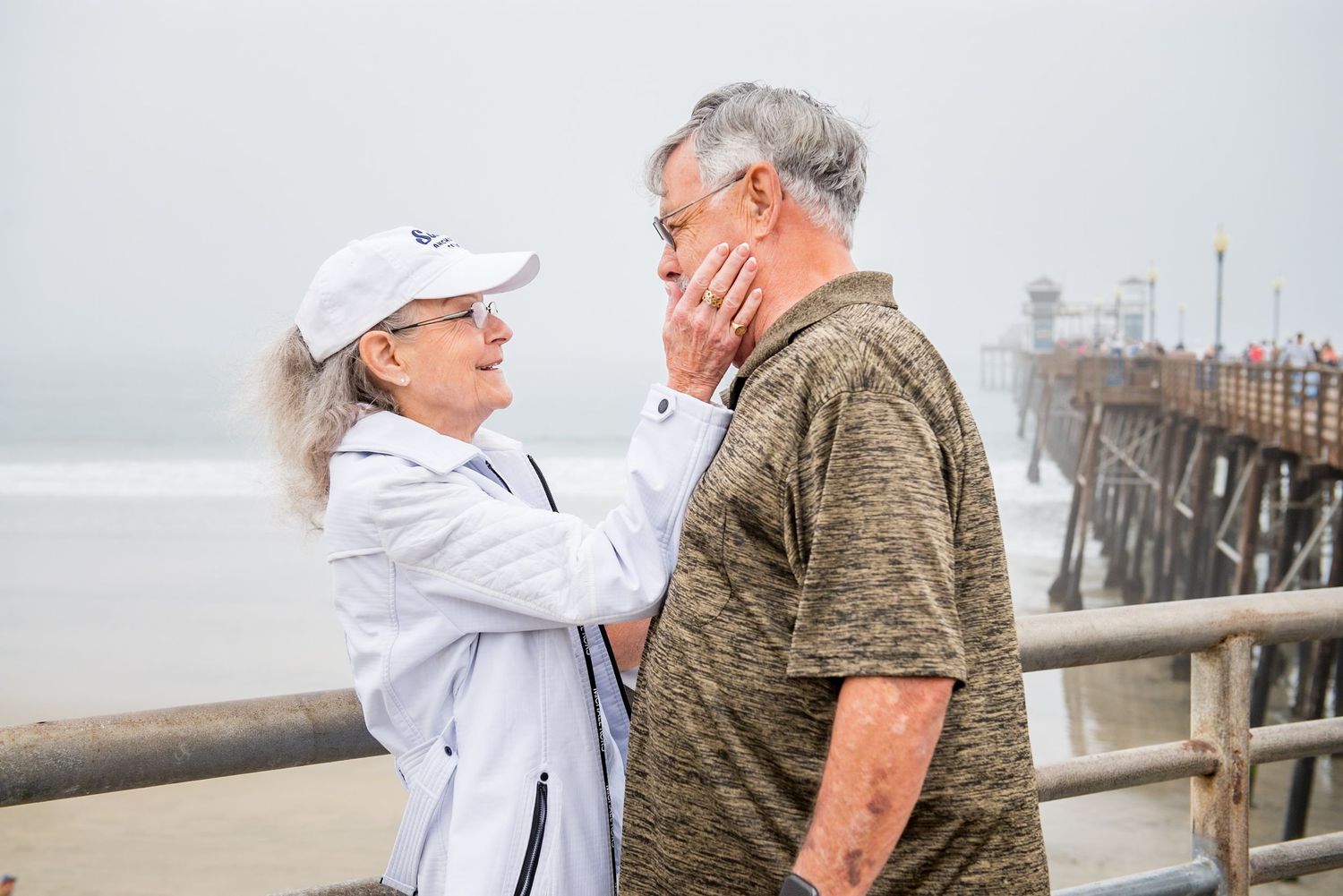 A couple shares a tender moment on a pier with a misty coastal background.