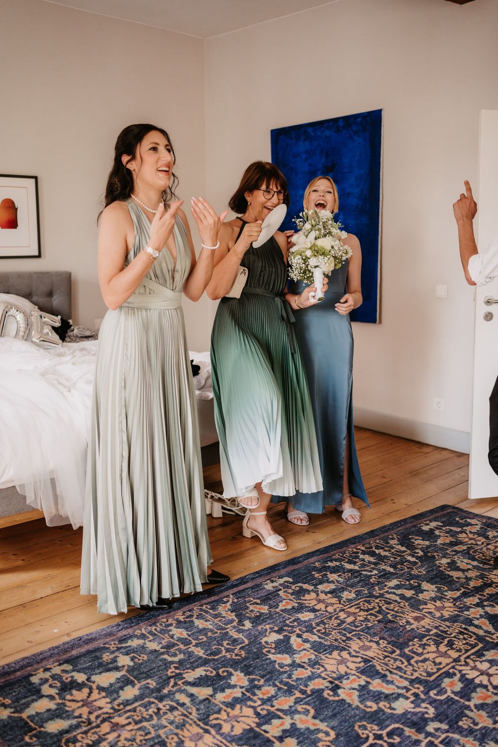 Wedding party in sage green and white dresses dancing together on a patterned blue rug in a bright room.
