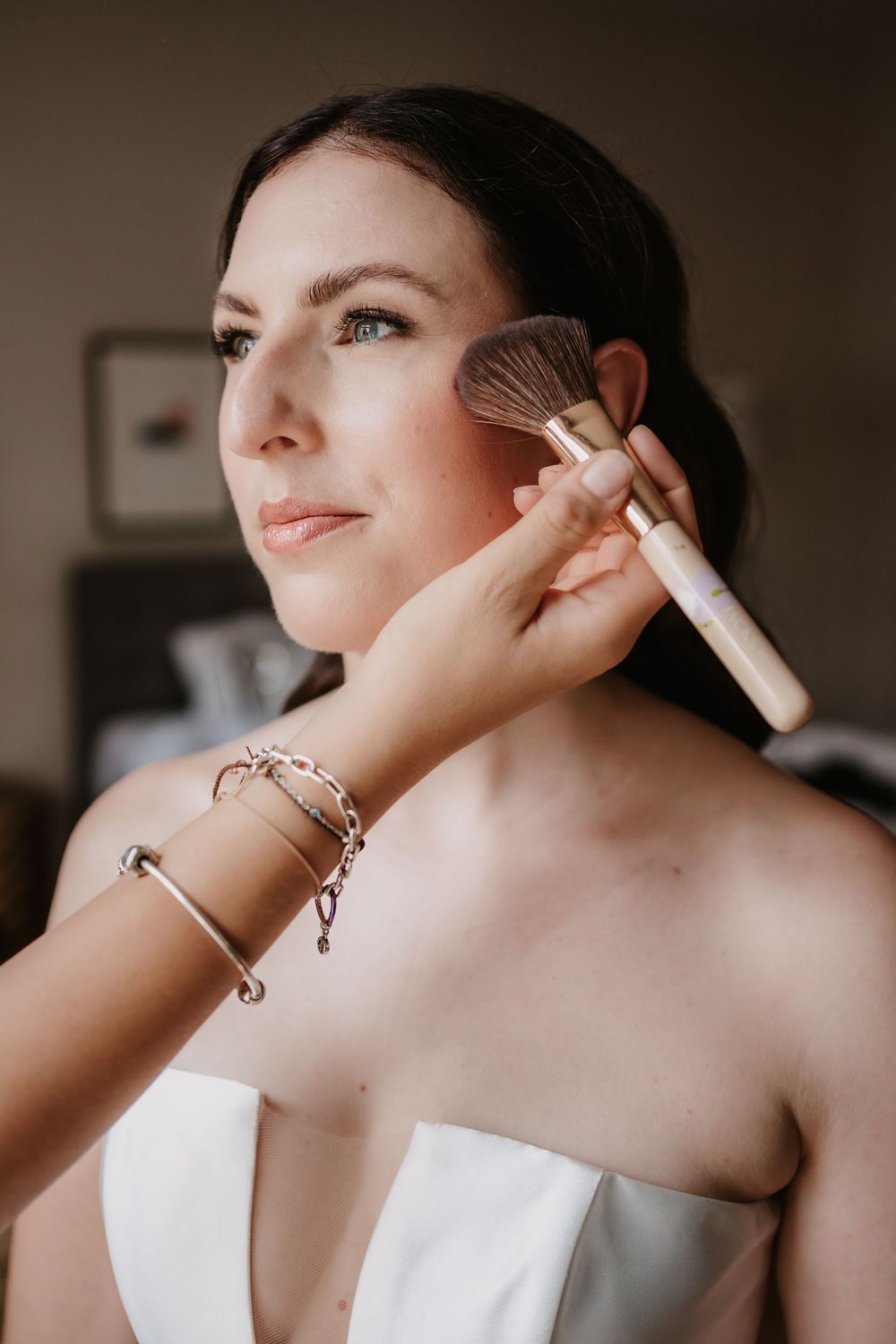 A person in a white garment gets ready for a special occasion with final makeup touches and adjustments.