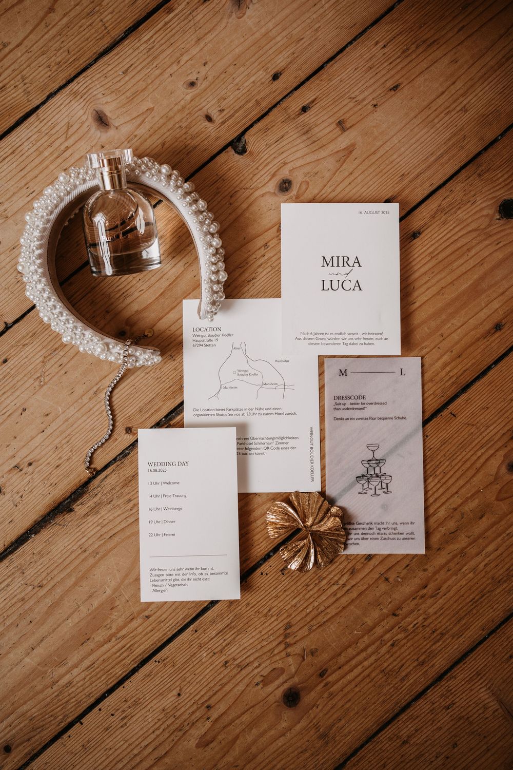 Wedding invitation suite with white cards and map details displayed on wooden floor alongside crystal headpiece.