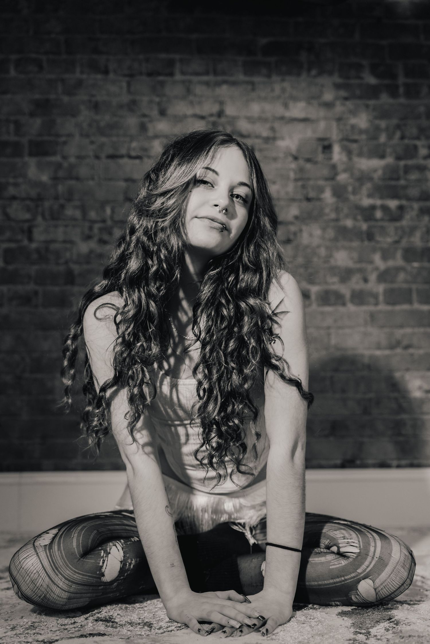 A dramatic black and white photo series shows a person with long curly hair lying on a textured floor against a brick wall.
