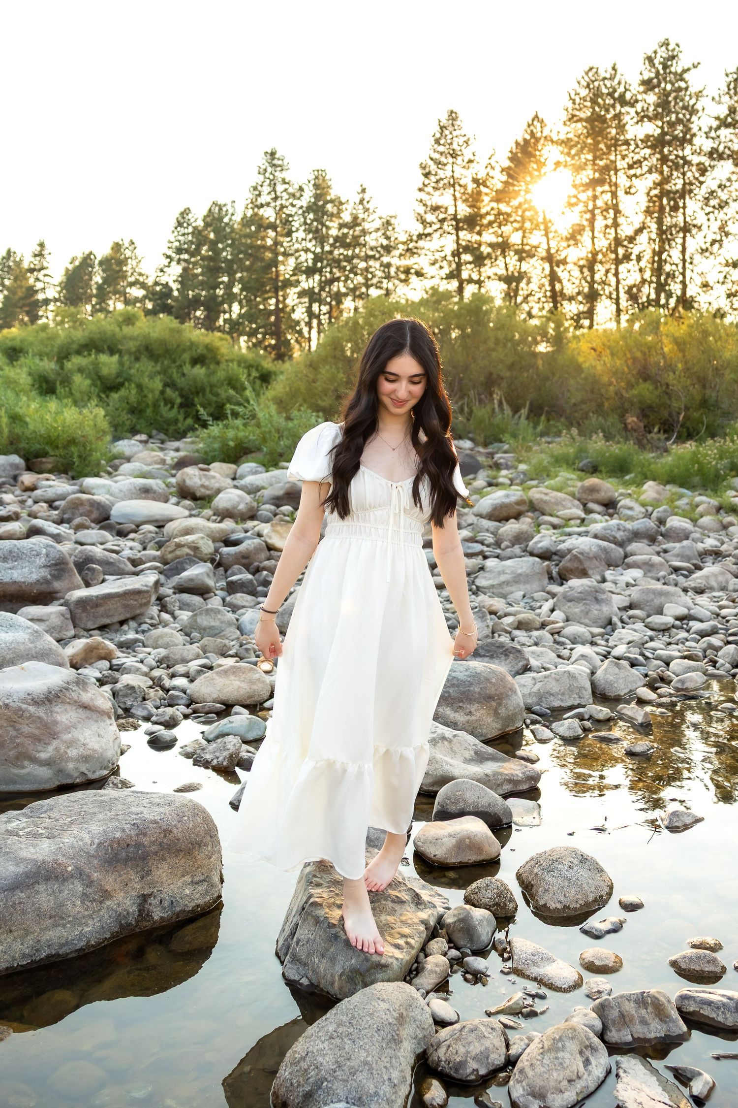 A series of photos showing someone in a flowing white dress sitting on rocks by a river at sunset.