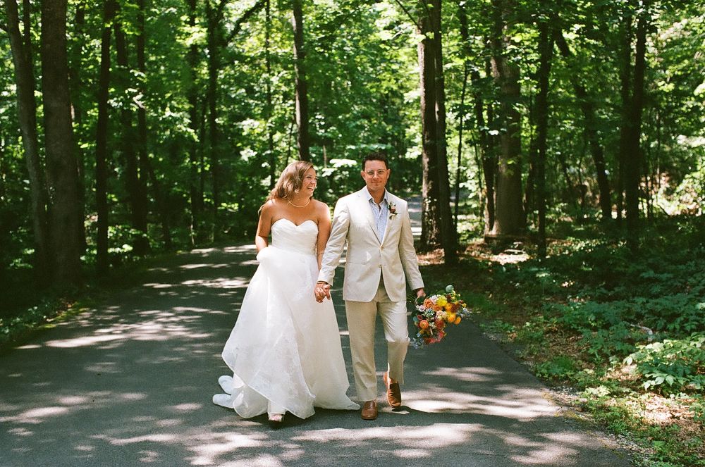 A couple walks together on a sunlit forest path surrounded by lush green trees on their wedding day.