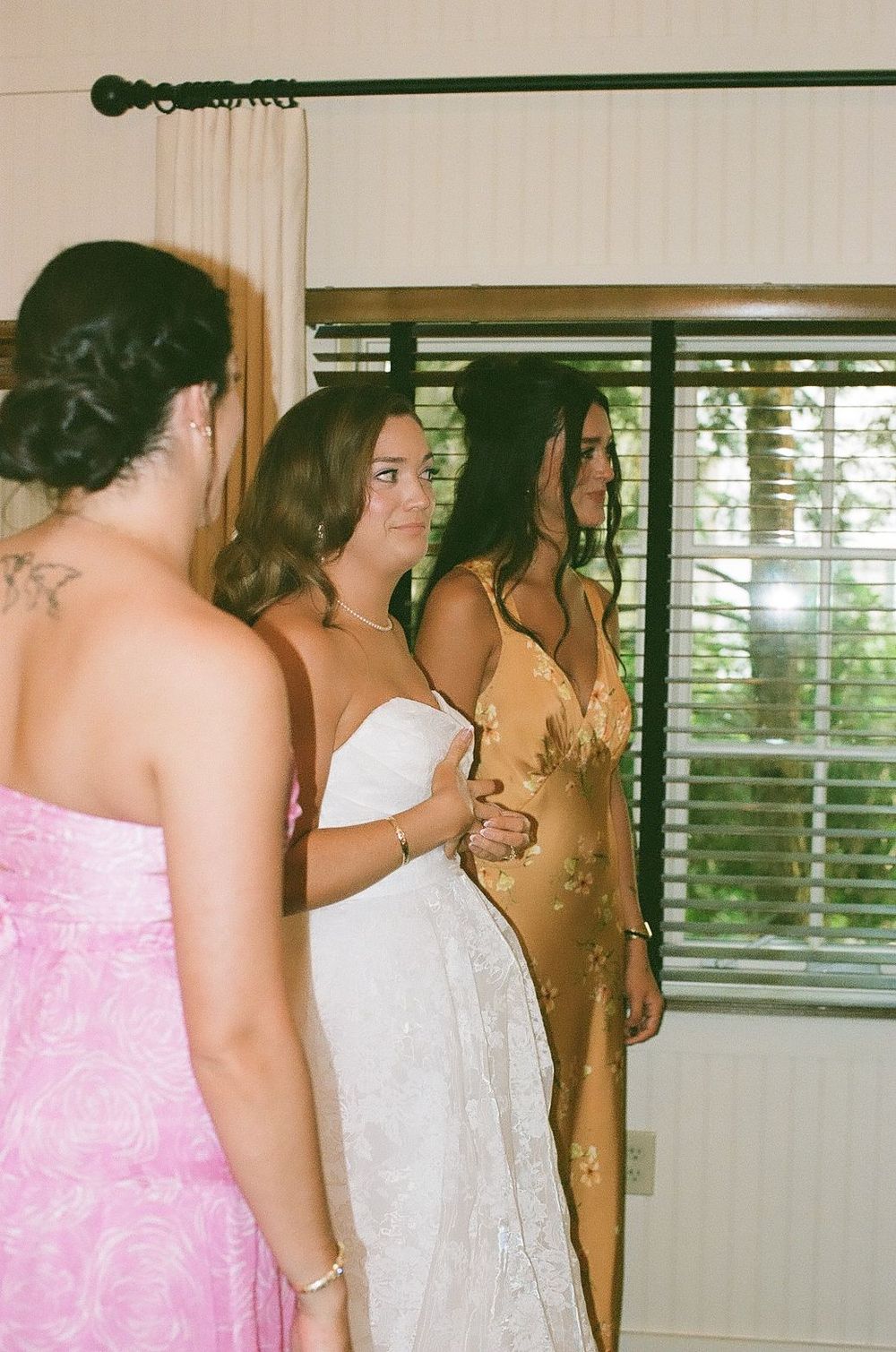 Three women in formal dresses stand together getting ready for a special occasion.