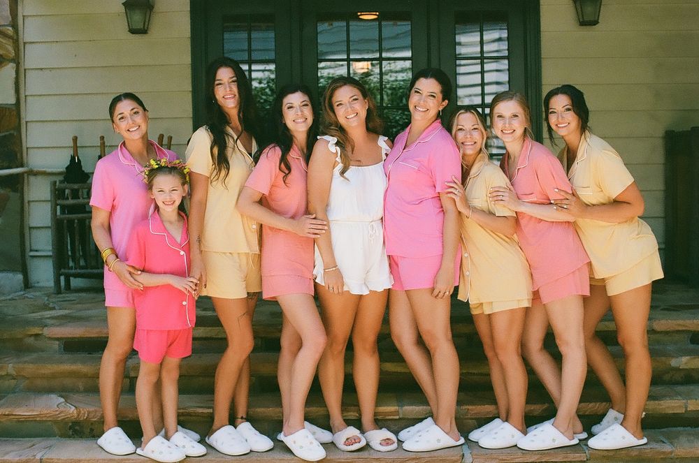 A group wearing matching pink outfits poses together on a porch during what appears to be a special event.