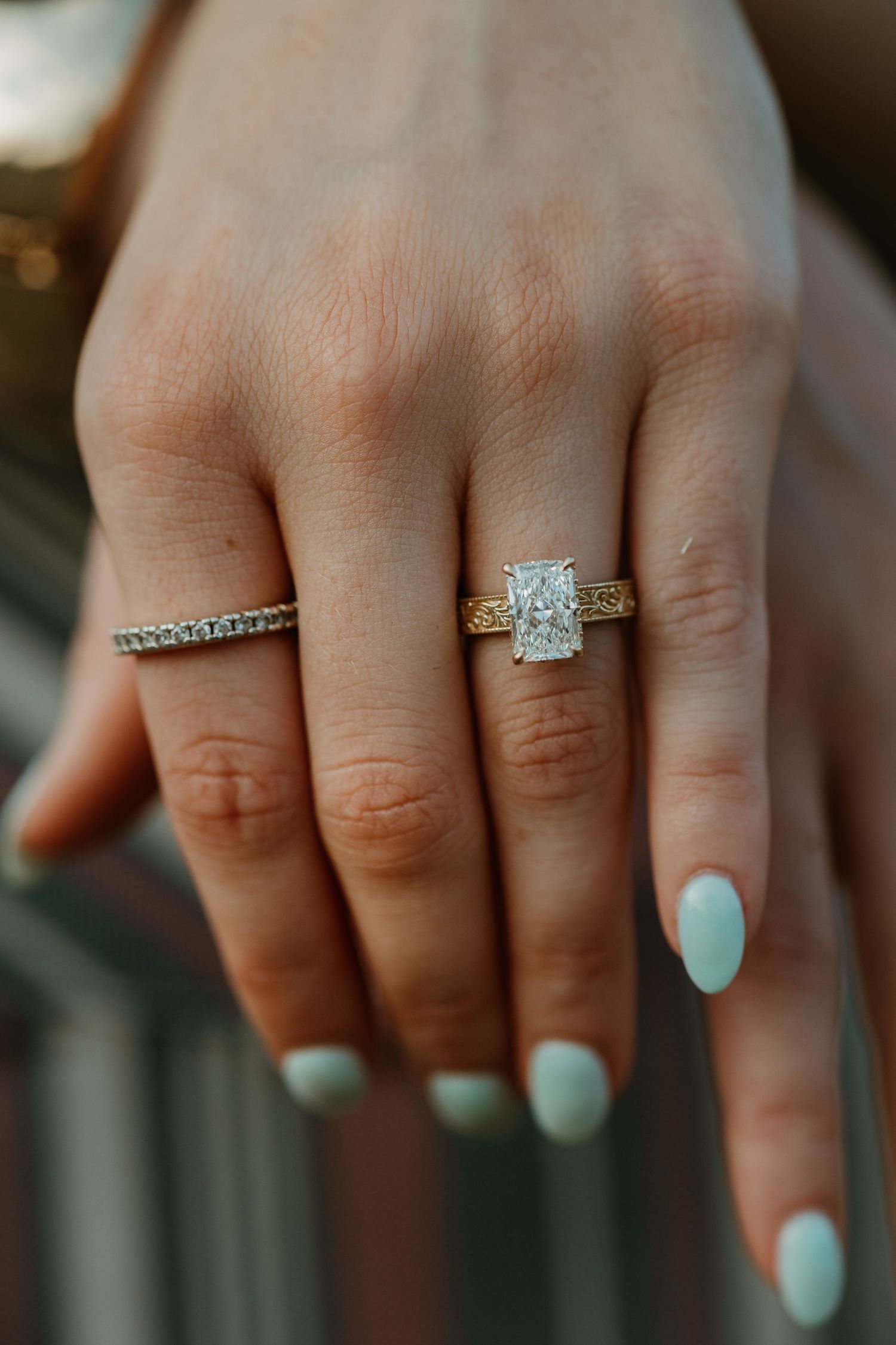 Close-up of hand wearing two sparkly diamond rings and mint green nail polish on fingers.