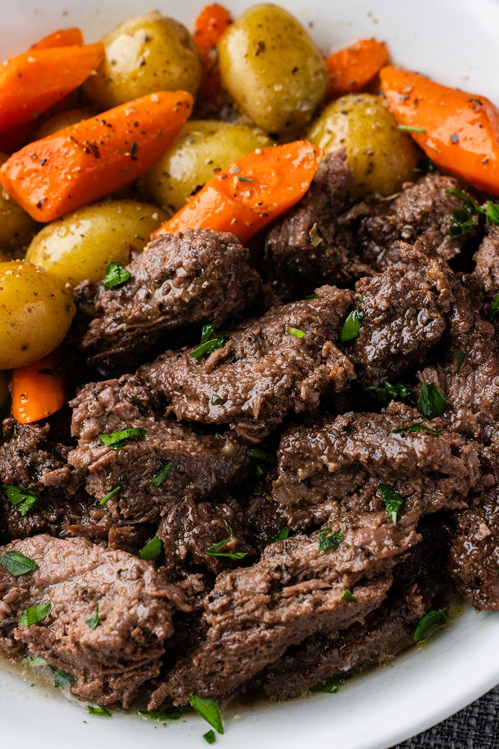 Tender braised beef served with roasted carrots and potatoes garnished with fresh herbs on a white plate.